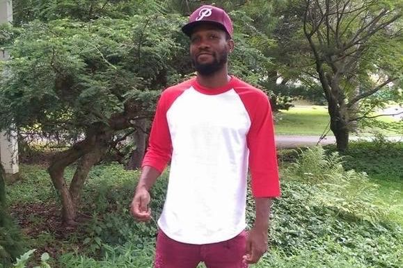 Maurice Gordon smiles in a photograph; he is wearing a maroon and white t-shirt, a maroon hat, and red pants